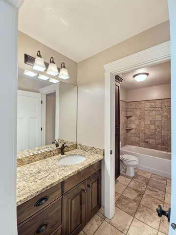 Jack and Jill Bathroom featuring a granite vanity with dark wood cabinetry, a rectangular mirror, and a three-light fixture