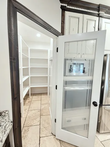 Walk-in pantry with extensive shelving, glass-paneled door, and tile flooring