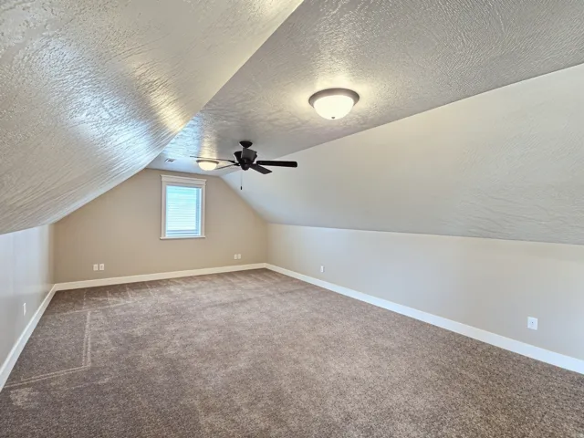Sloped ceilings with textured finish, neutral wall paint, and plush carpet flooring a large and open living space ready for you to fill it with great memories.