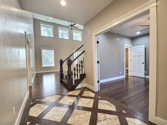 Vaulted entry featuring a decorative floor inlay, wood flooring, and a detailed staircase