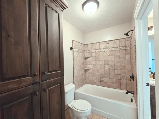 Built-in custom cabinetry, tile flooring, full-size bathtub, tiled shower surround with built-in shelving, and dark-finish fixtures