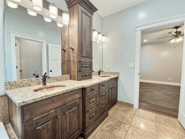 Dual vanity with granite countertops, rich wood cabinetry, integrated storage tower, copper sinks and bronze-finish fixtures