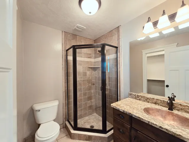 On sutie bathroom featuringTiled shower enclosure with a dark-framed glass door and a vanity with a copper sink.