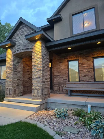 Brick facade with arched entry, integrated soffit lighting, stepped concrete porch, and a gravel landscape bed