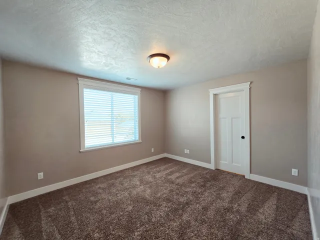 Neutral wall finishes, textured ceiling, window with blinds, panel door with dark hardware, and carpet flooring with walk in closet and dedicated on-suite bathroom.