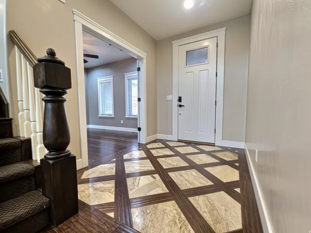 Entryway featuring a patterned tile and wood flooring, a  front door with transom window, and a staircase with a dark wood newel post and white balusters.