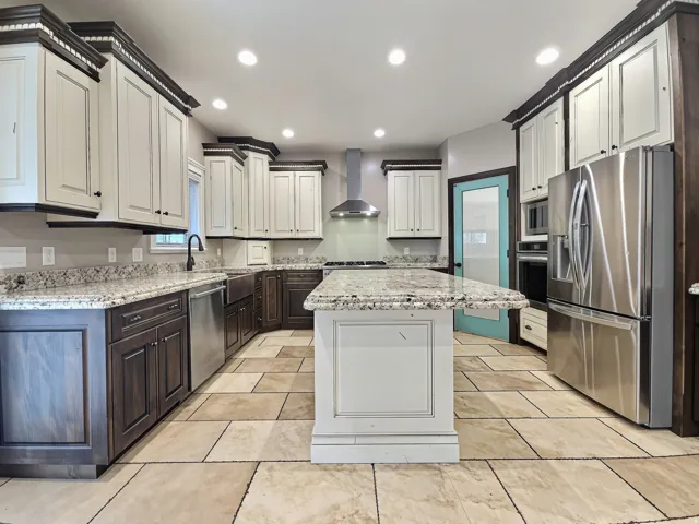 Kitchen featuring an expansive center island, sculpted edge granite countertops, tile flooring, stainless steel appliances, and two-tone cabinetry
