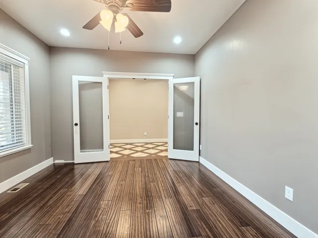 Main Floor office featuring wood flooring, recessed lighting, ceiling fan light fixture, double French doors, and white trim with a picture window.