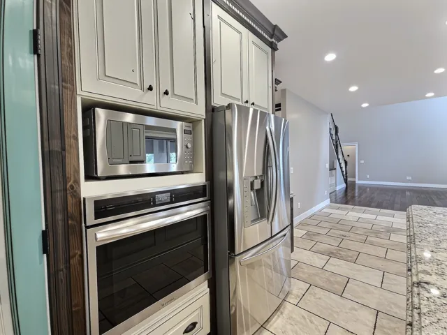 Stainless steel appliances, built-in microwave, wall oven, and light-toned cabinetry complement the granite-finish countertop and tile flooring