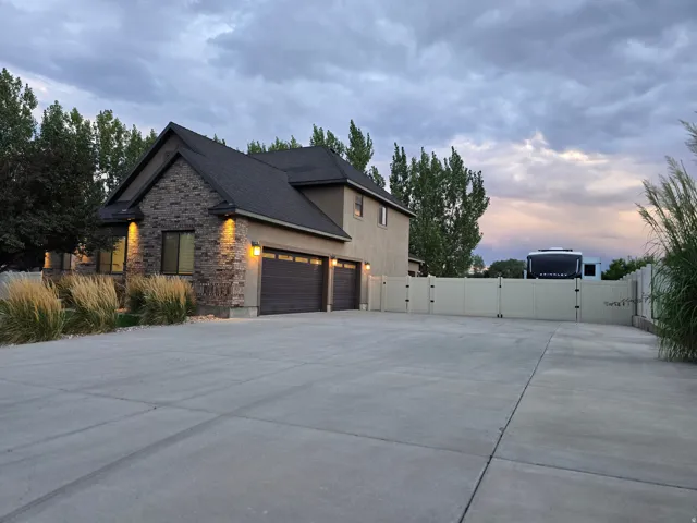 Multi-car garage with sectional doors, stone accent facade, stucco exterior, extensive concrete driveway, and privacy fencing with large gate.
