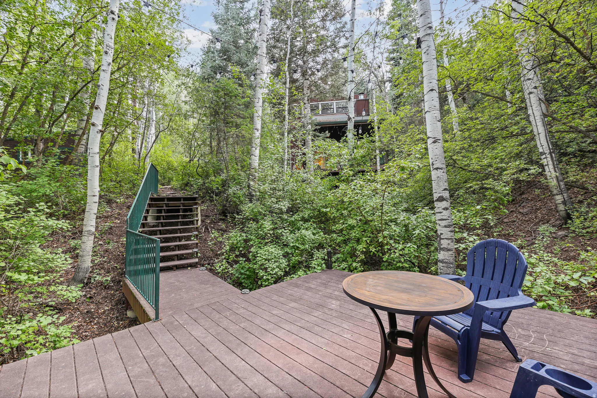 Expansive wood-finish decking with an integrated staircase and green metal railing, surrounded by mature trees