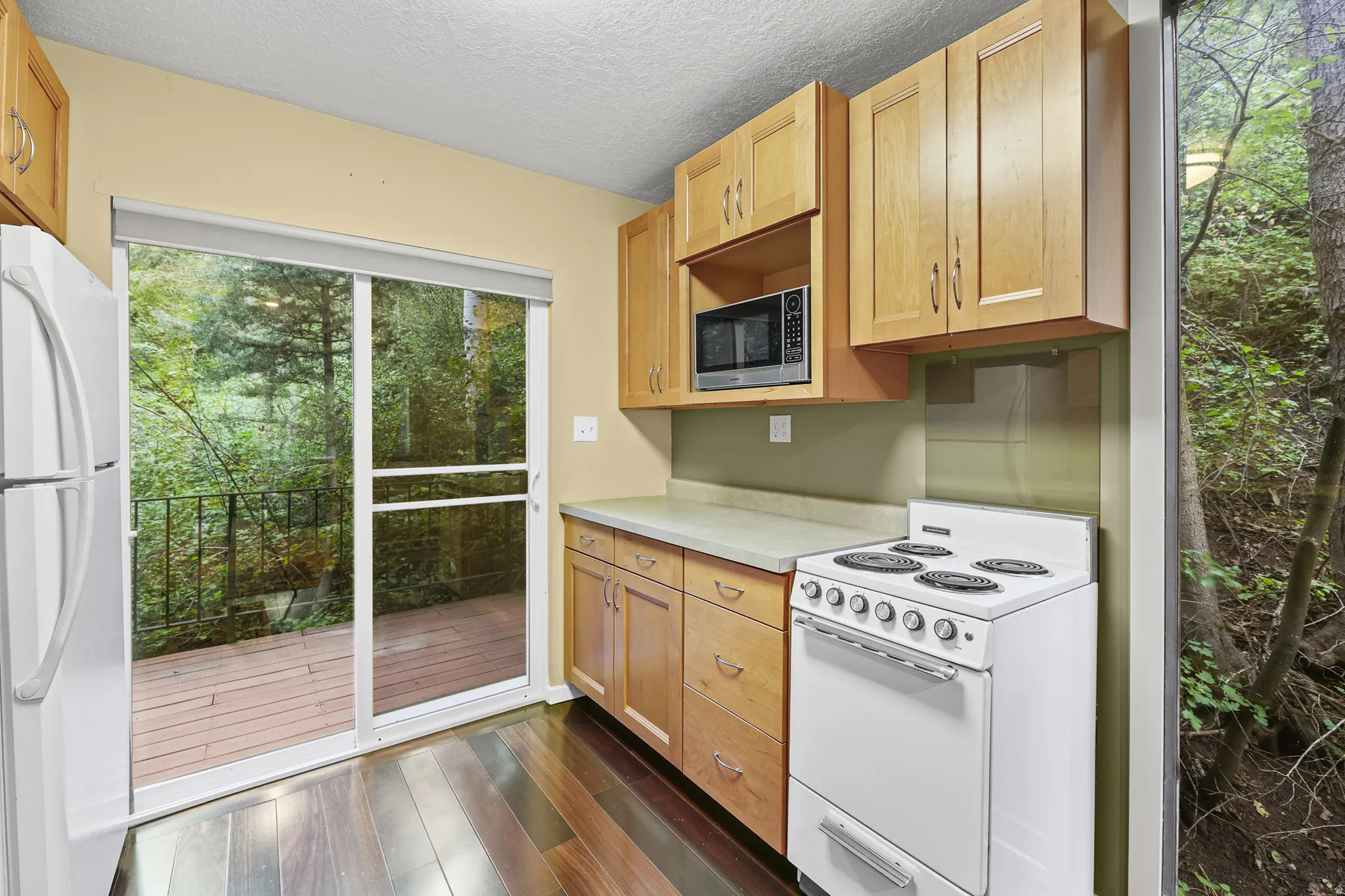 Kitchen featuring wood-finish flooring, light wood cabinetry, white appliances, and a sliding glass door to a deck