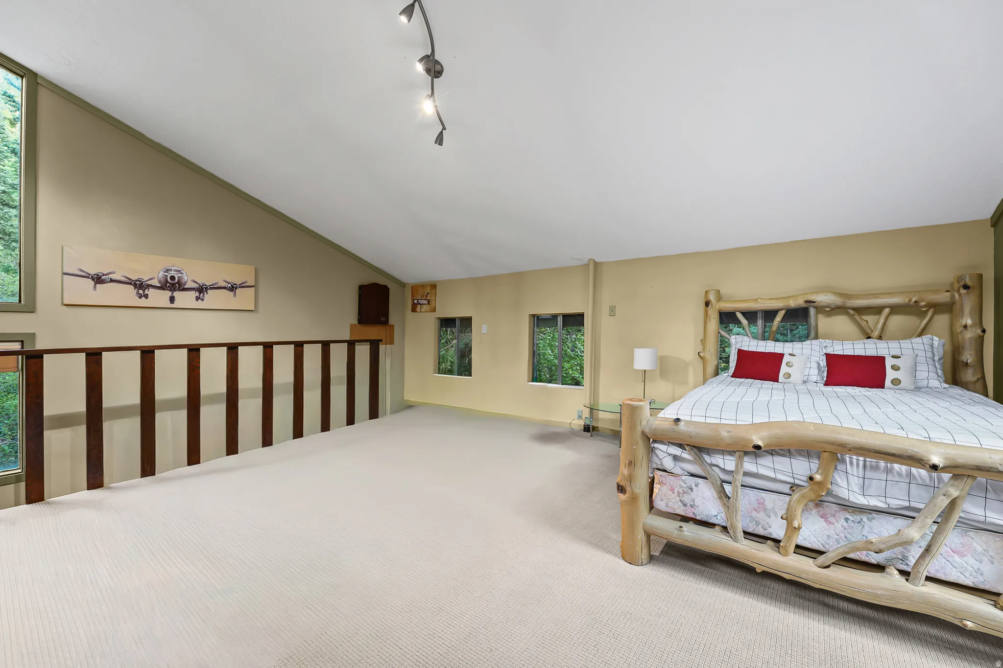 Loft space featuring sloped ceilings, track lighting, a wood railing, and multiple windows*Photo has been edited to take out pool table*