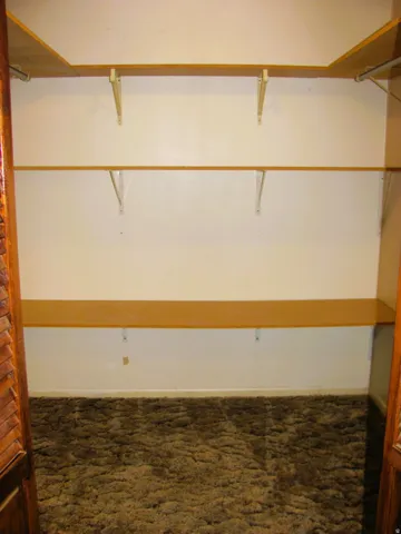 Built-in wood-finish shelving with metal supports, wall-mounted hanging rods, and wood-finish louvered bi-fold doors