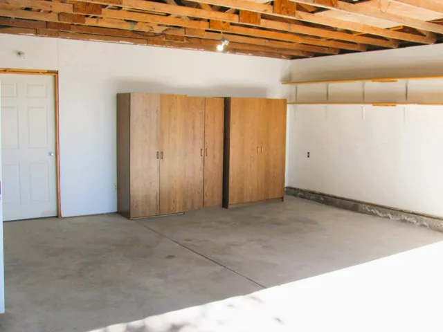 Concrete flooring, visible ceiling joists, white interior door, wood-finish cabinetry, and built-in shelving