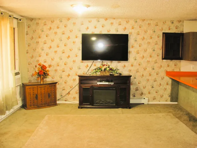 Wall-mounted television with decorative wallpaper, built-in electric fireplace, and a wood-finish corner cabinet