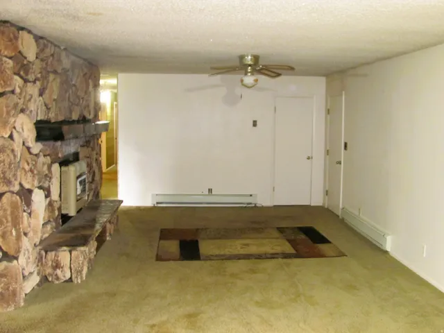 Stone-clad fireplace with mantel and hearth, wall-to-wall carpeting, and ceiling fan with light fixture
