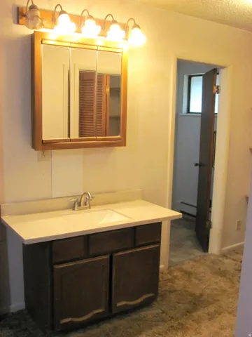 Vanity with integrated sink and chrome-finish faucet, framed medicine cabinet, and overhead lighting fixture
