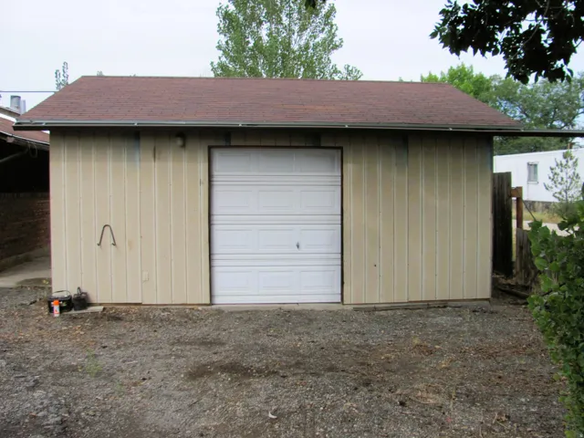 Detached structure featuring a white sectional garage door, vertical siding, and a brown shingle roof