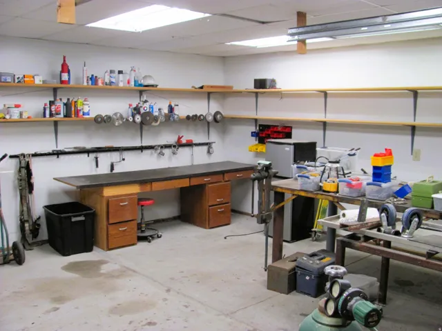 Fluorescent ceiling lighting, built-in shelving, concrete flooring, and a workbench with integrated drawers
