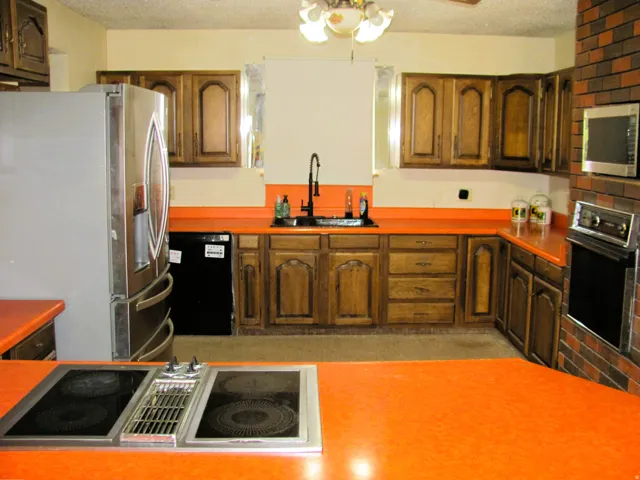 Kitchen featuring wood-finish cabinetry, integrated cooktop, built-in oven, and brick-look wall paneling