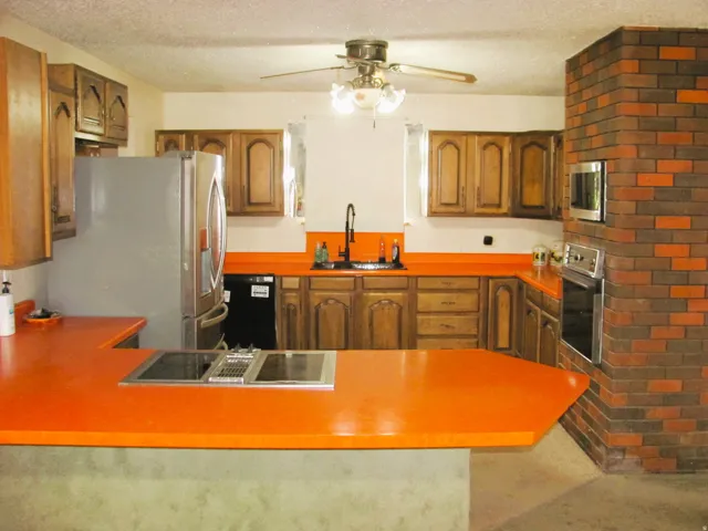 Kitchen featuring wood cabinetry, integrated stainless steel appliances, vibrant orange countertops, and a brick-finish partial wall