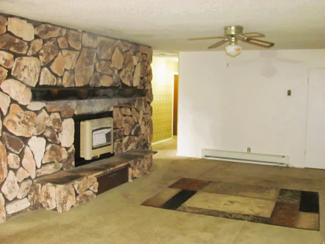 Stone fireplace with built-in hearth seating, wall-mounted heating unit, and ceiling fan
