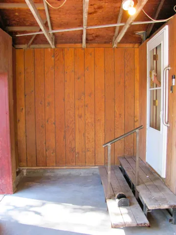 Wood-paneled wall, concrete flooring, exposed ceiling joists, and a partial wooden ramp with a metal handrail