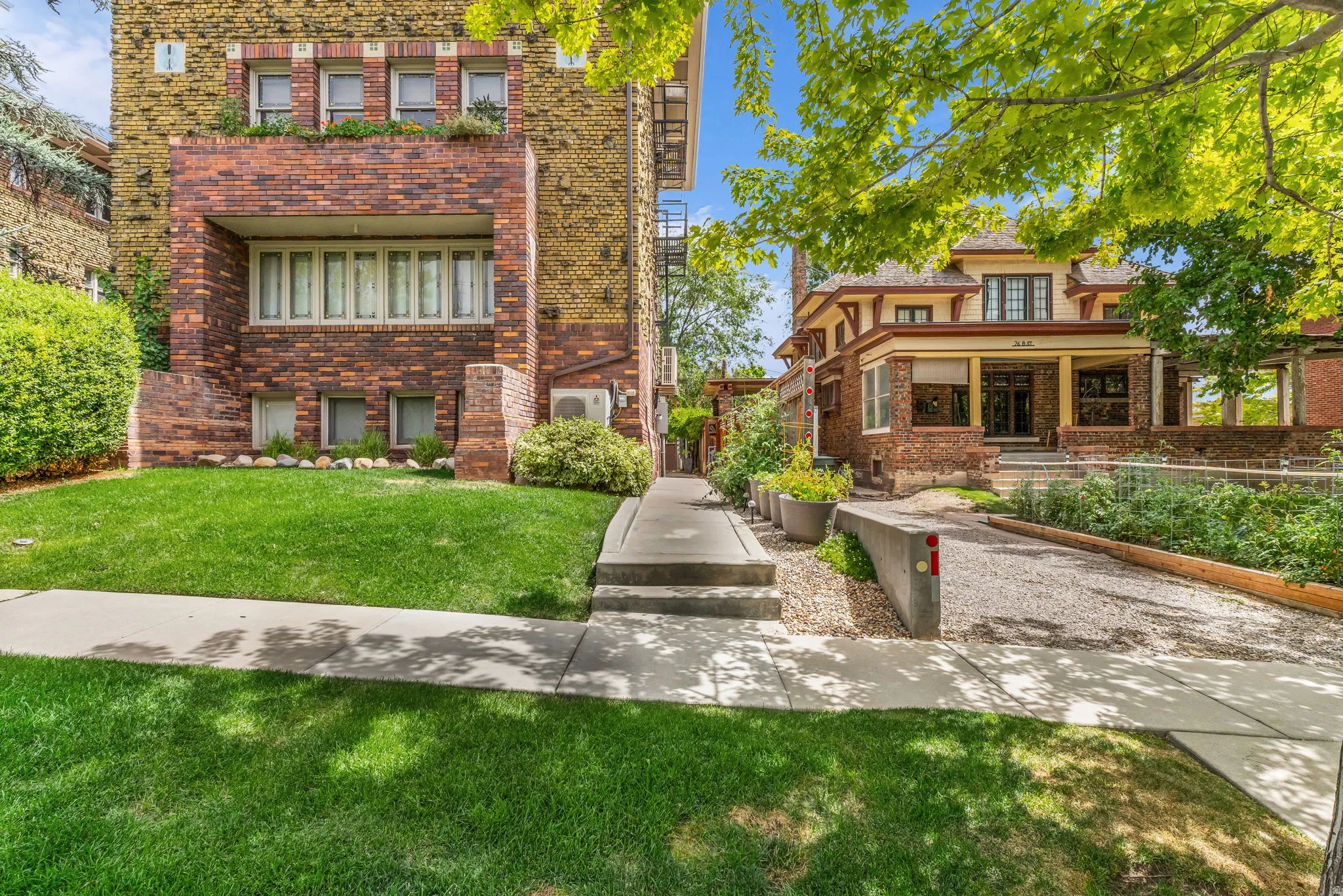 Brick facade with a recessed balcony, multiple window configurations, concrete pathway, and an adjacent gravel driveway