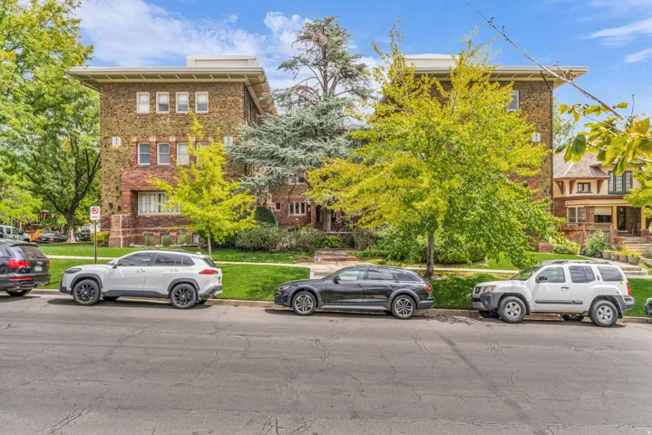 Brick facade architecture with a prominent cornice, surrounded by mature trees and manicured lawns