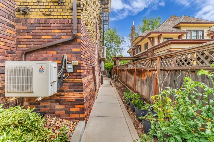 Brick exterior with a concrete walkway, mature wood fencing, and planted container gardens
