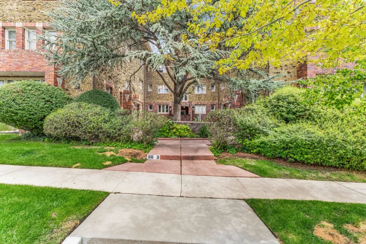 Brick exterior construction featuring multiple windows, mature trees, and landscaped shrubbery