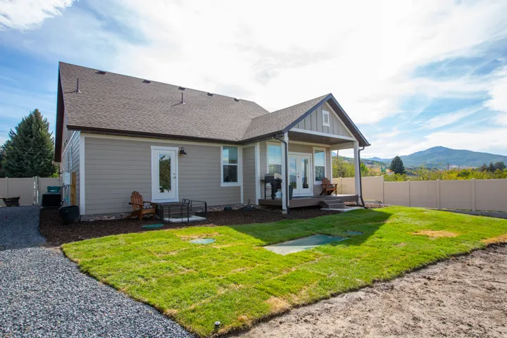 Expansive backyard featuring a manicured lawn, gravel pathway, and a covered patio with a dark wood-finish deck