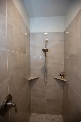 Custom tiled doorless shower enclosure featuring a handheld showerhead, brushed nickel fixtures, recessed lighting, and integrated corner shelving