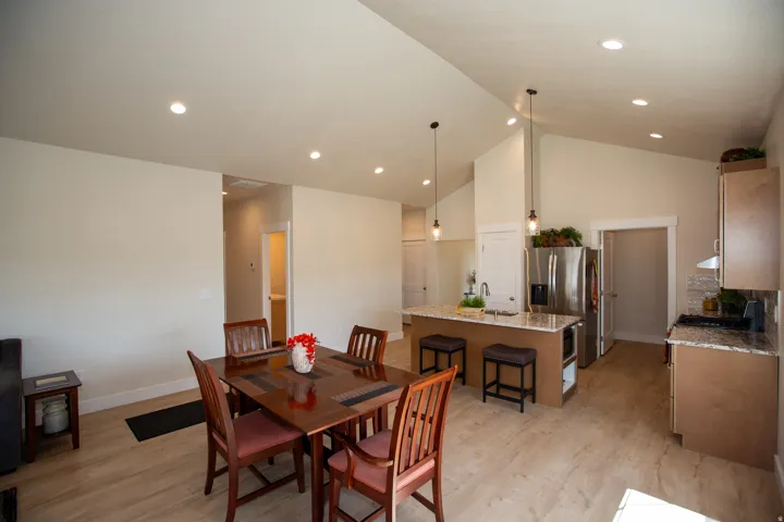 Open-concept living space featuring wood-finish flooring, vaulted ceilings, recessed lighting, and a kitchen island with stone countertops