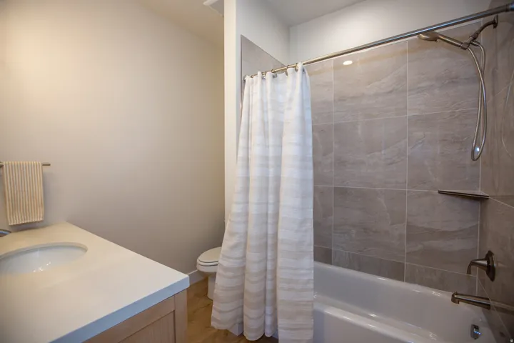 White single-basin sink with a light-toned countertop, wood-finish vanity, and a custom tiled shower-tub combination with a built-in shelf