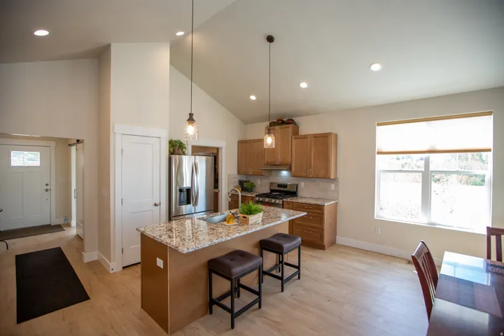 Vaulted ceiling with recessed lighting, kitchen island with seating, stainless steel appliances, wood-finish flooring, and a large window