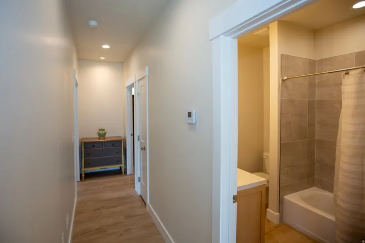 Recessed ceiling lighting, wood-finish flooring, and a full bathroom with a tiled shower surround and a single vanity