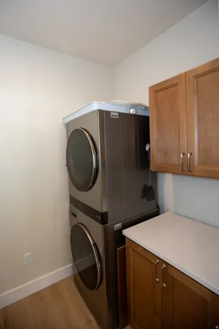 Built-in stacked laundry appliances, wood-finish flooring, white walls, wood cabinetry, and a light-toned countertop