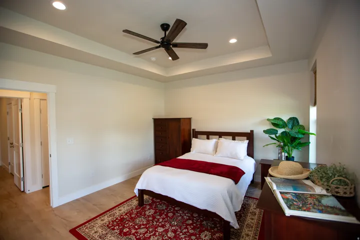 Tray ceiling with recessed lighting fixtures, wood-finish ceiling fan, wood-finish flooring, and white trim