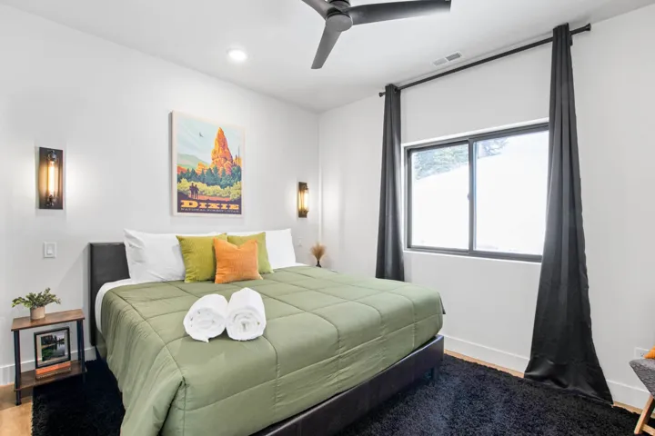 Bright bedroom showcasing a ceiling fan, recessed lighting, large windows with black curtains, wood-finish flooring, and a dark area rug