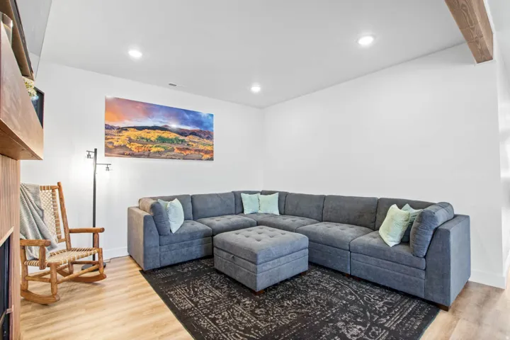 Spacious recreation room featuring a modular sectional layout, recessed ceiling lighting, exposed beam accents, wood-finish flooring, and a patterned area rug anchoring the seating arrangement