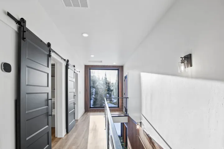 Wood-finish flooring, recessed ceiling lighting, wall-mounted light fixtures, dark-finish barn doors, and large picture window