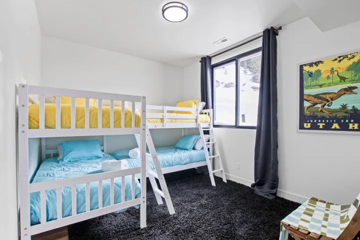 Bright bedroom featuring dual bunk beds with white wooden frames, blue bedding, and integrated storage