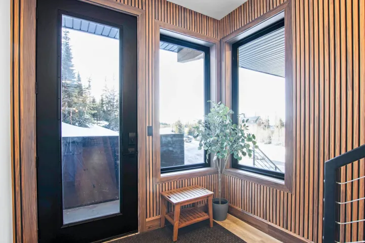 Full-light entry door with black frame, wood-slat accent wall, and multiple black-framed windows