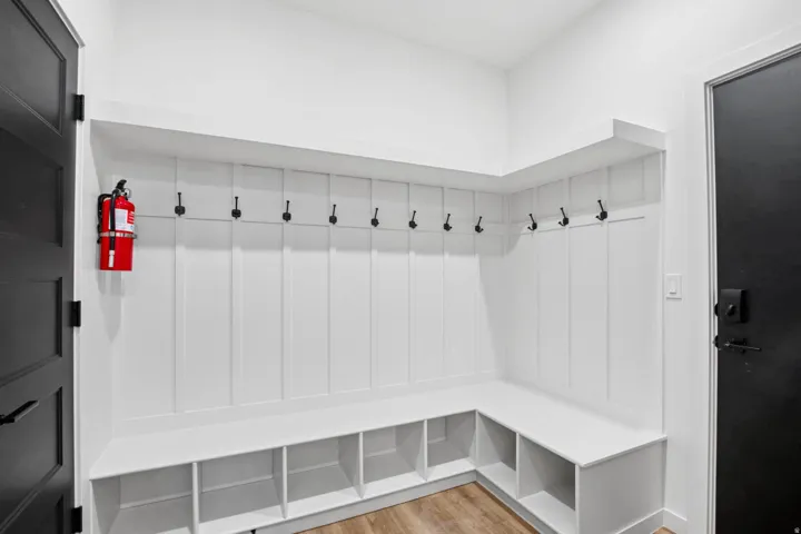 Built-in bench seating with cubbies, white vertical paneling, black wall hooks, wood-finish flooring, and a black paneled door