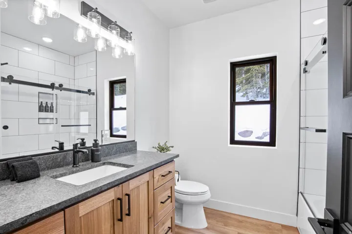 Wood-finish flooring, single vanity with a stone countertop, white rectangular vessel sink, and black wall-mounted faucet