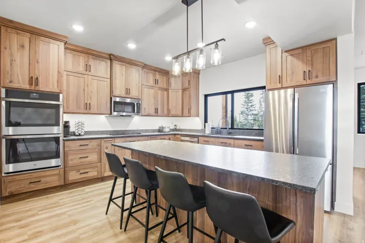 Well-appointed kitchen featuring wood cabinetry, stainless steel appliances, a large island with a stone-finish countertop, and wood-finish flooring