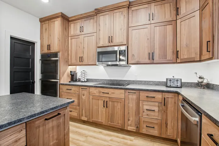 Wood-finish cabinetry with matte black hardware, dual stainless steel wall ovens, stainless steel microwave, integrated stainless steel dishwasher, and a spacious countertop