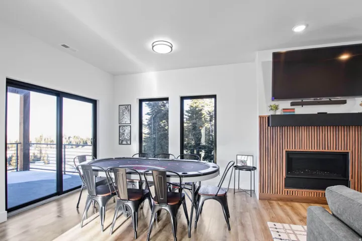 Expansive sliding glass doors, multiple large windows, a sleek fireplace with a slatted wood-finish surround, and light wood-finish flooring